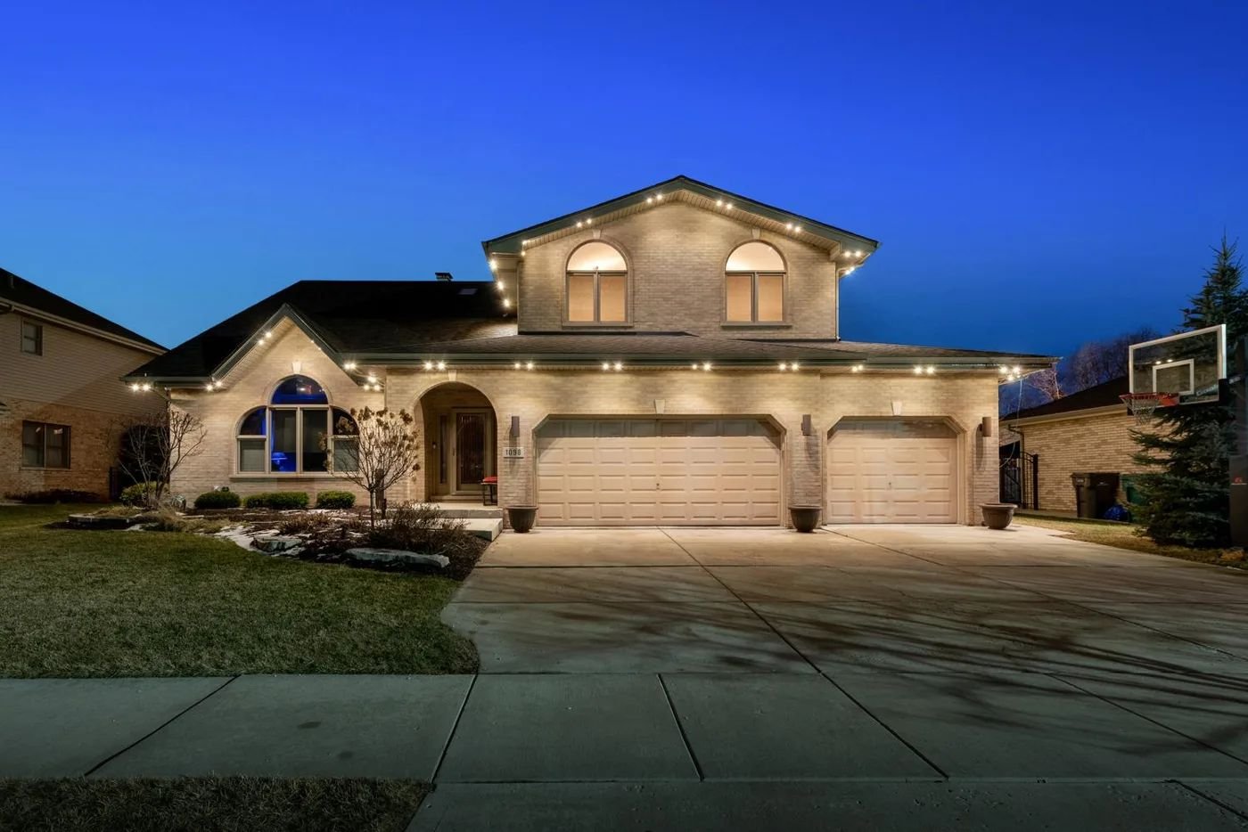 Two-story brick home at dusk with permanent warm-white lights along the eaves and gables